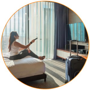 woman sitting on bed in hotel with remote in hand looking at TV screen
